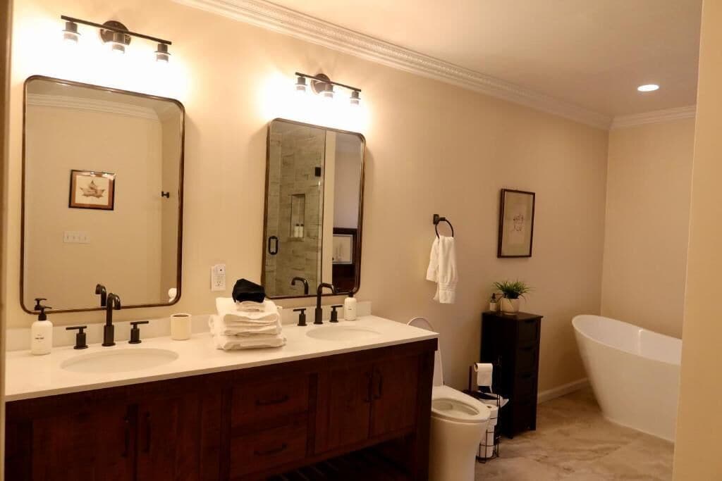 A bathroom with two sinks, a large mirror, a bathtub, and a toilet.