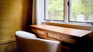 A room with a wooden desk, a chair, and a window with a view of trees.