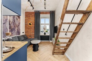Ein modernes Wohnzimmer mit Backsteinwand, einer Holzleiter, einer Couch, einem runden Couchtisch und einem an der Wand montierten Fernseher.