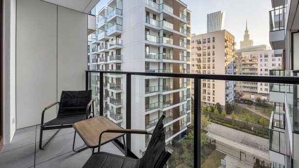 En balkon med udsigt over moderne lejlighedskomplekser, en stol og et bord.