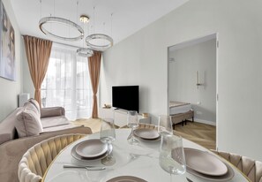 Una sala moderna con una mesa redonda para comer, un sofá, un televisor y una puerta que da a otra habitación.