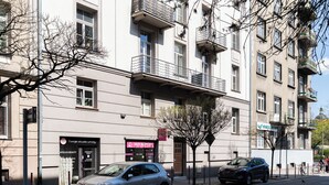 Un edificio de varios pisos con balcones, un coche estacionado y una tienda con letreros.