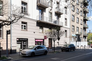Ein mehrgeschossiges Gebäude mit Balkonen, einem parkenden Auto und einem Geschäft mit Beschilderung.