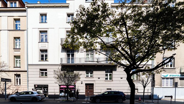 Un edificio de varios pisos con fachada plana, una entrada visible y un árbol en primer plano.