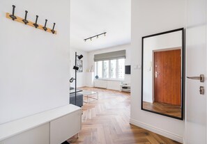 Un intérieur moderne avec un plancher en bois, un porte-manteau blanc fixé au mur, un grand miroir et une porte dotée d’un cadre noir.