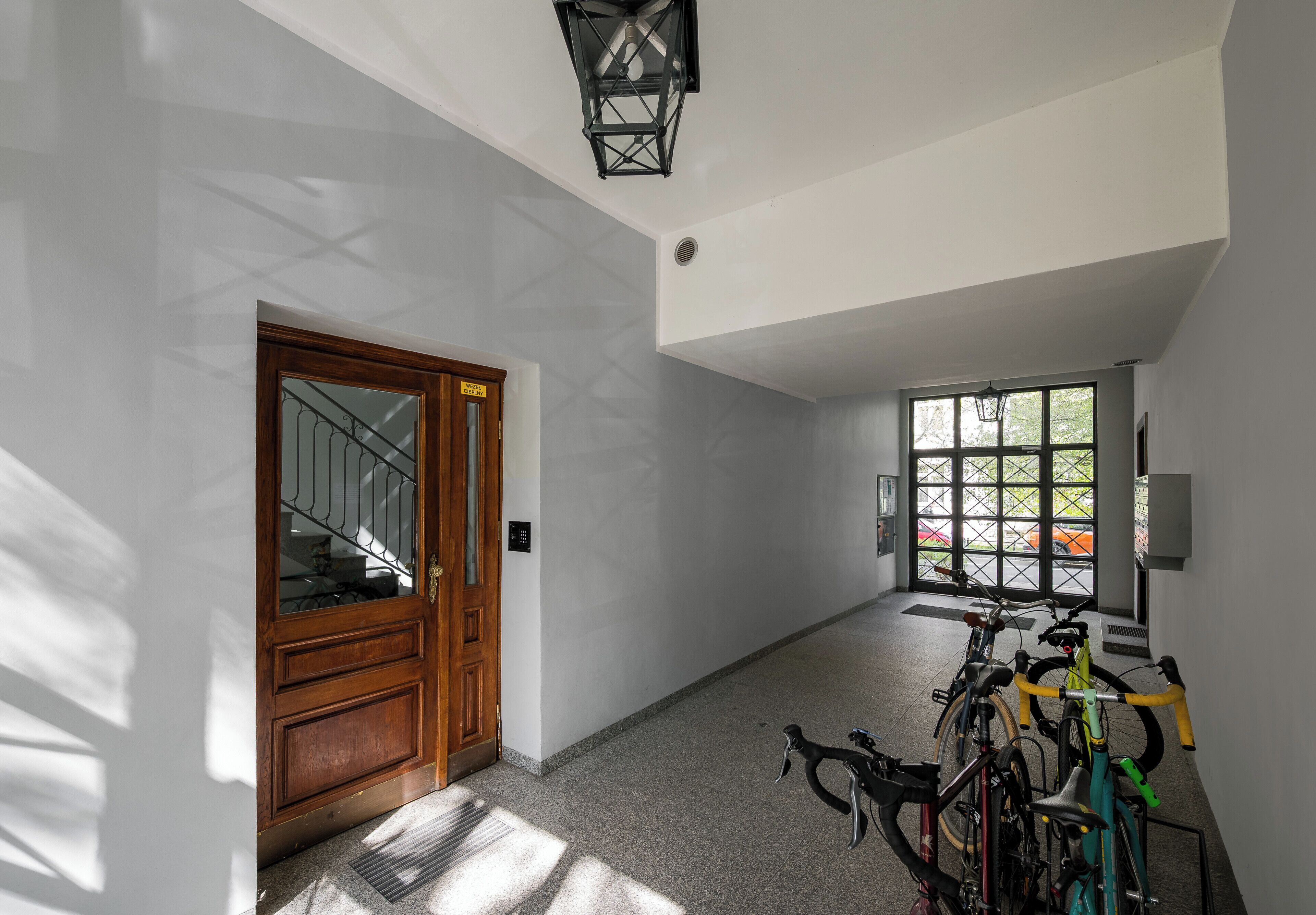 Un pasillo con una puerta de madera, un aparcamiento para bicicletas y una ventana con vistas a árboles.