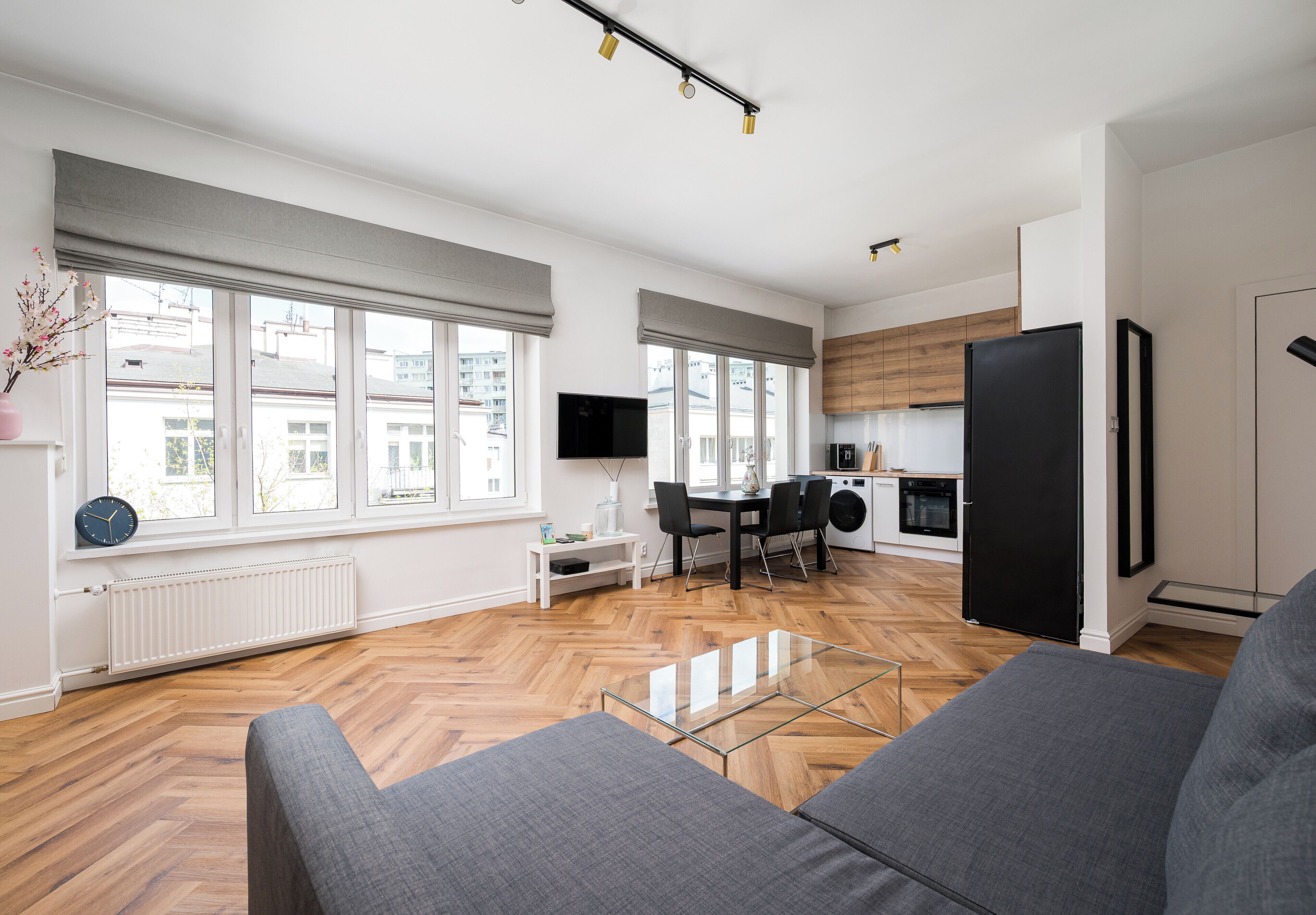 A modern apartment with a dining area, kitchen, and living room with a sofa and a glass coffee table.
