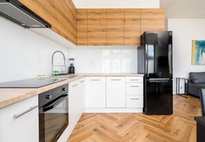Une cuisine moderne avec des meubles blancs, un réfrigérateur noir et un parquet en bois disposé en chevrons.