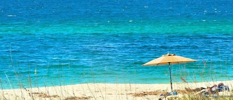 A beach with clear blue water, a sandy shore, and a beach umbrella.