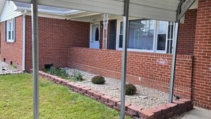 A covered outdoor area with a brick building, a concrete pathway, and a small garden area.