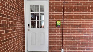 A red brick exterior with a white door, a small step leading to the entrance, and a utility box on the wall.