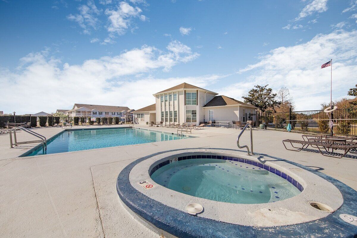 A swimming pool area with a hot tub, lounge chairs, and a building with large windows.
