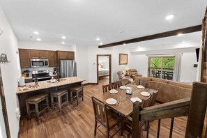A modern kitchen with built-in appliances, a dining area with wooden furniture, and a view of the outdoors.