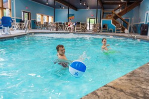 An indoor swimming pool with clear water, a lifeguard chair, and a blue and white ball.