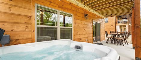 Een houten chalet met een jacuzzi, een eethoek en een overdekt terras.