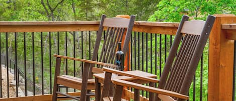 A wooden deck with two Adirondack chairs and a table, surrounded by a wooden railing.