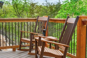 A wooden deck with two Adirondack chairs and a table, surrounded by a wooden railing.