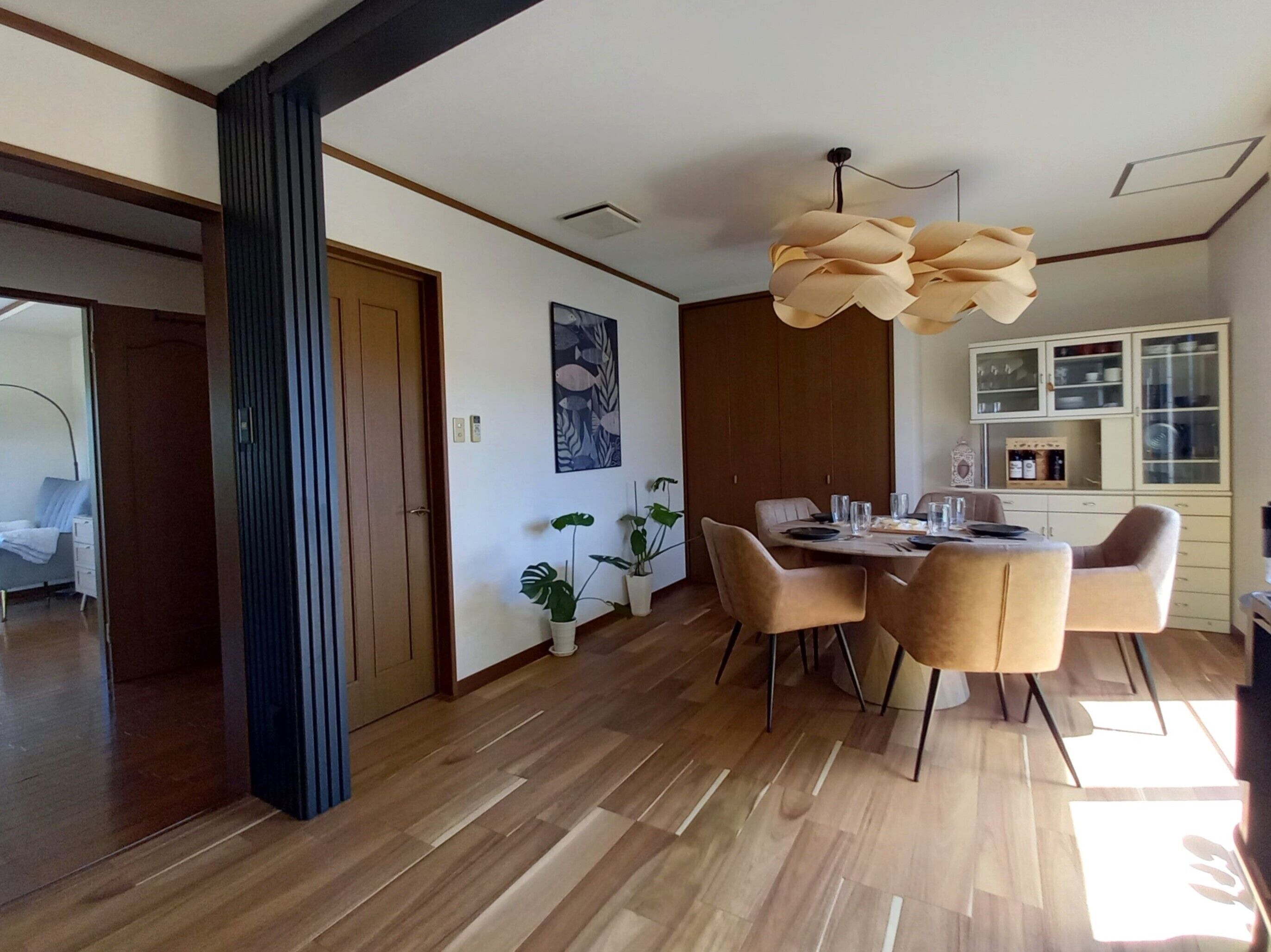 Un'area pranzo moderna con pavimento in legno, un tavolo rotondo e quattro sedie. Si nota una porta in legno e una pianta in vaso sulla parete.