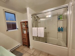 Un baño con ducha acristalada, repisa de madera con toallas y artículos de aseo.