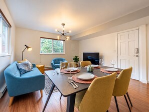 Un coin repas avec une table dressée pour quatre personnes, un canapé bleu et un téléviseur en arrière-plan.