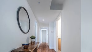 A hallway with wooden flooring, a wooden bench with a bowl and plant, and a mirror on the wall.