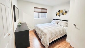 A bedroom with a bed, a window with blinds, a bedside table, and a wall decoration.