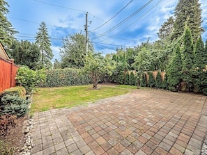 A paved backyard with a brick patio, a small grassy area, and a red building.