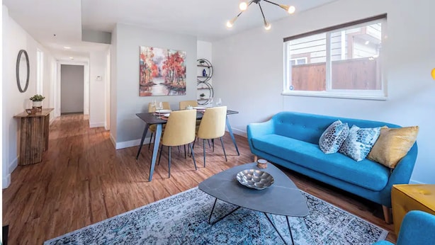 A modern living room with a blue sofa, dining table, and a unique ceiling light fixture.
