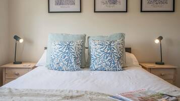 Una cama bien tendida con dos almohadas iguales, una lámpara de noche a cada lado y un patrón antiguo enmarcados en la pared.
