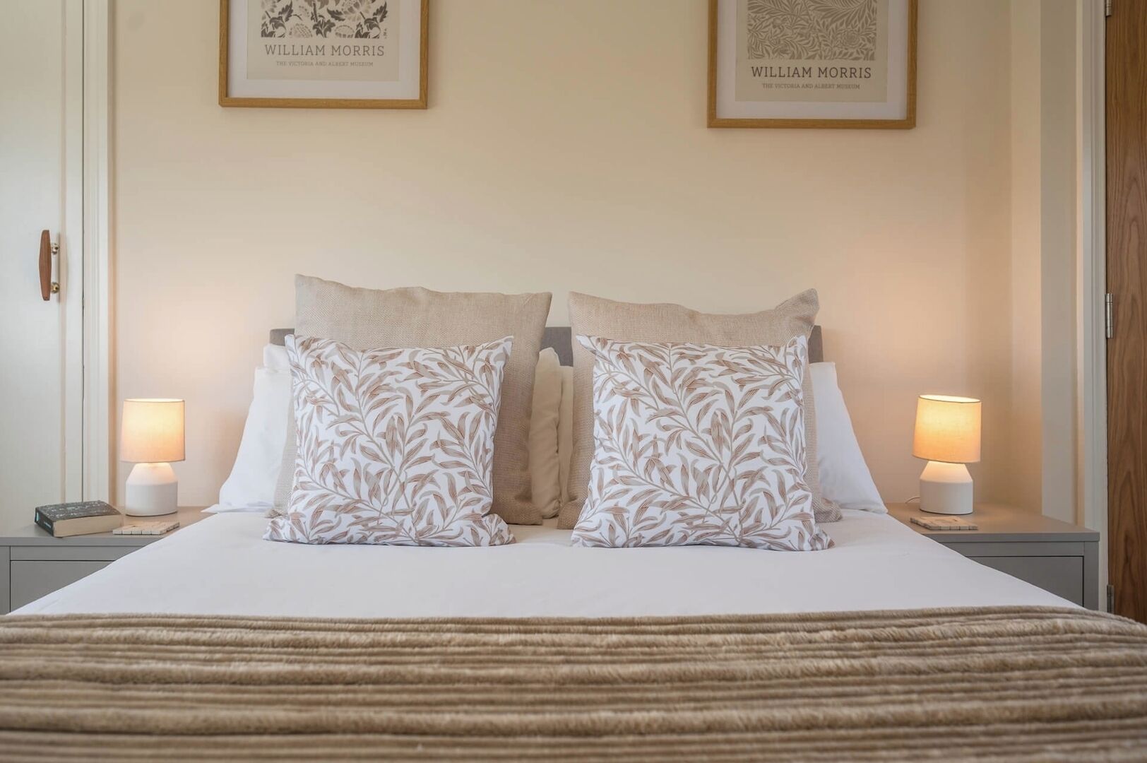 A neatly made bed with two pillows, two bedside lamps, and two framed pictures on the wall.