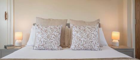 A neatly made bed with two pillows, two bedside lamps, and two framed pictures on the wall.