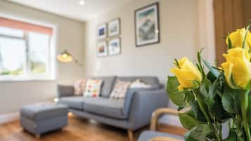 A living room with a grey sofa, a small ottoman, and a vase of yellow flowers.
