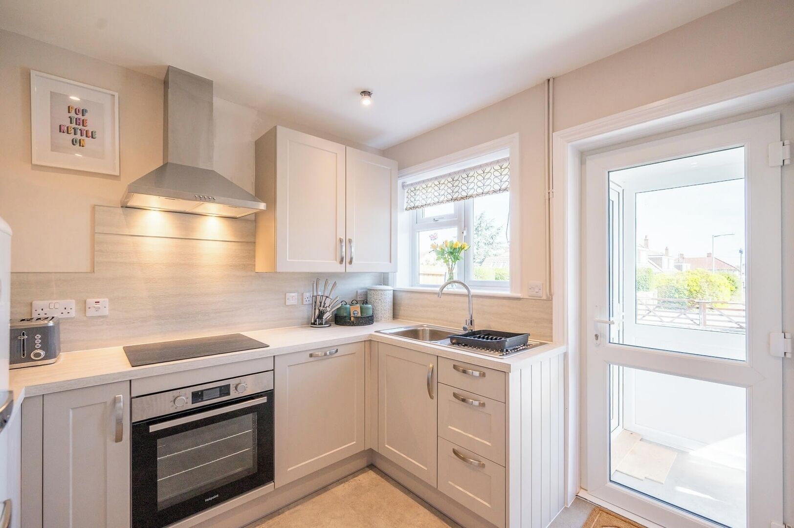 A modern kitchen with white cabinetry, a built-in oven, a stainless steel range hood, and a window with a view of the outside.
