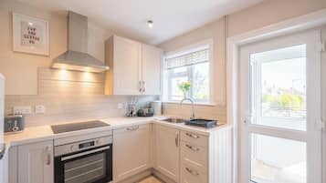 A modern kitchen with white cabinetry, a built-in oven, a stainless steel range hood, and a window with a view of the outside.