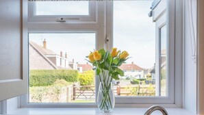 A window with a view of a residential area, a clear sky, and a vase with flowers on the windowsill. - 105 Saxmundham Road, Aldeburgh (Aldeburgh)