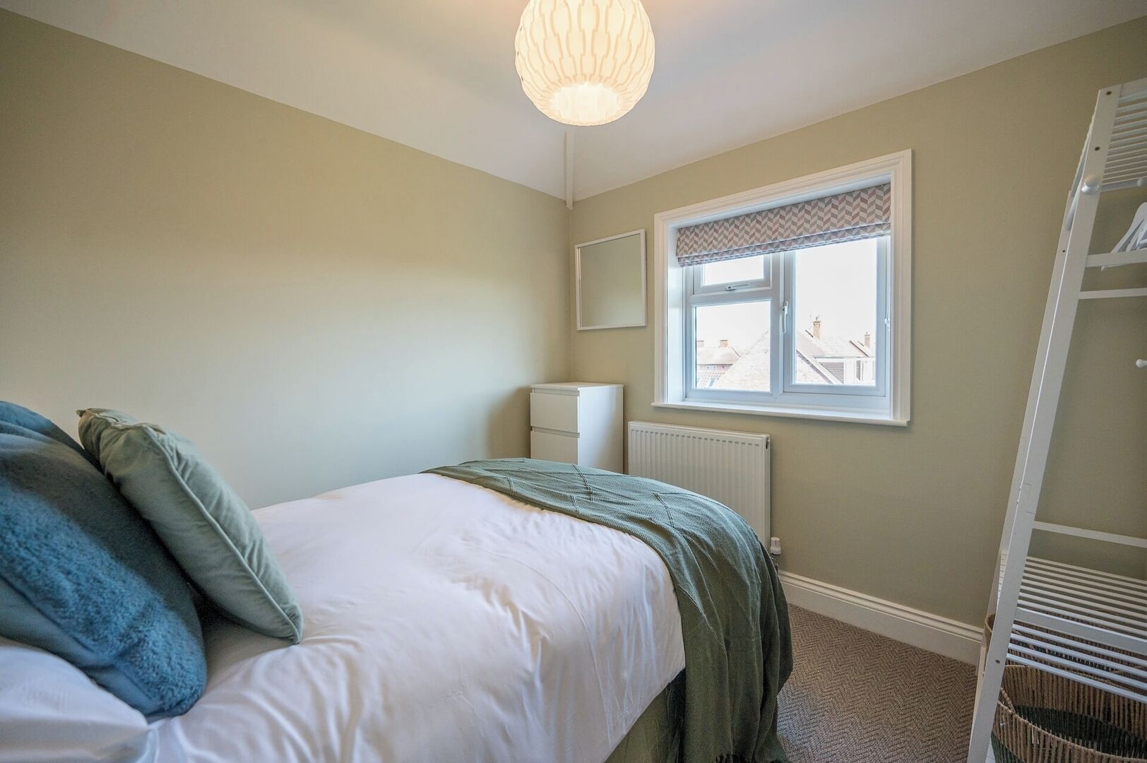 Une chambre à coucher avec un lit, un radiateur, une fenêtre donnant sur un beau paysage et une armoire blanche.