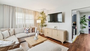 A modern living room with a sofa, coffee table, TV, and a plant. - 8 BR • Theater • Game Room • Fire Pit • Sleeps 15 (Birmingham)
