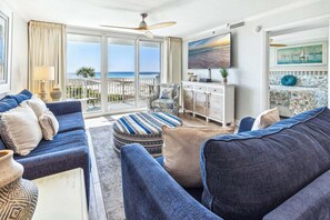 A living room with a sofa, ottoman, and armchair, a television, and a painting. - 312 Gorgeous Gulf Views w/ 25’ Private Balcony ~ Pool ~ Hot Tub ~ Book Aug 10th (Destin)