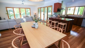 Una cocina moderna con armarios de madera, un comedor con mesa y sillas de madera, y ventanas amplias que ofrecen vistas al exterior.