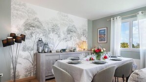 En matplats med ett bord dukat för två personer, en väggmålning och ett fönster med gardiner.