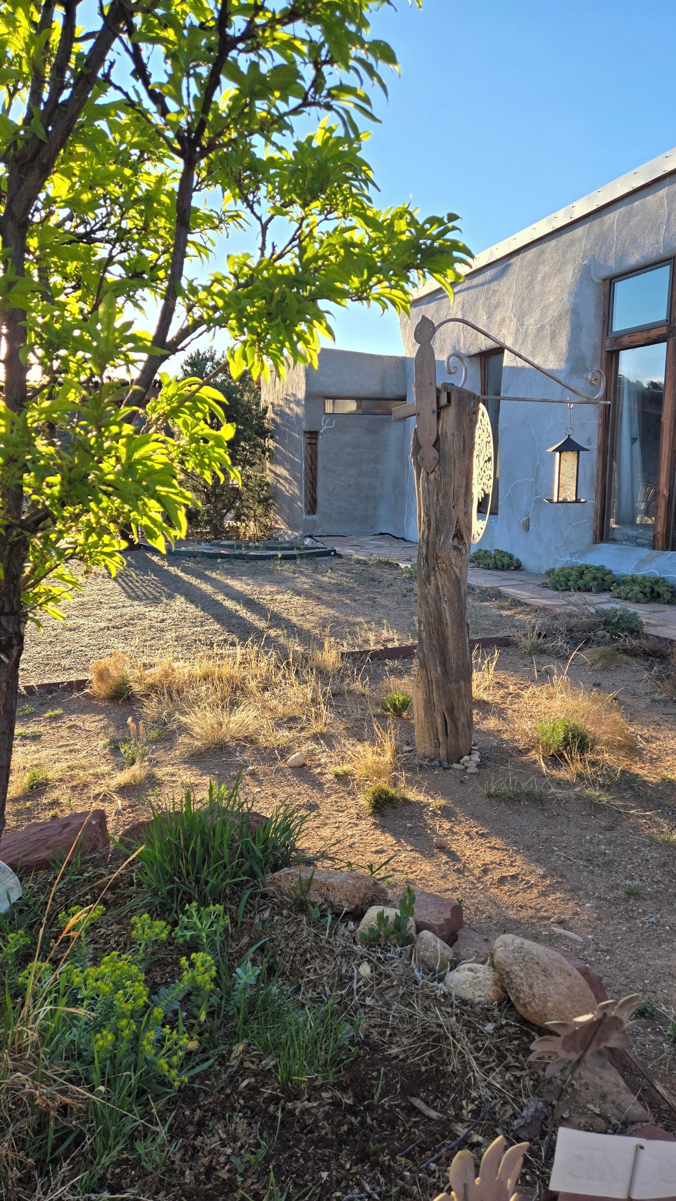 A garden area with a wooden post, a metal bird feeder, and a building with large windows.