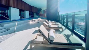 A rooftop pool area with sun loungers, a glass balustrade, and a view of the city skyline. - Luxury High-Rise Stay with Panoramic GC Views (Broadbeach)