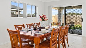 Un coin repas avec une table et des chaises en bois, un vase de fleurs et une vue sur une terrasse extérieure, accessible par une porte-fenêtre coulissante.