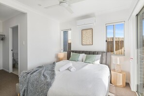 Un dormitorio con cama, ventilador de techo, unidad de aire acondicionado, ventana y puerta que da a un baño.