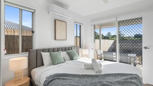 Un dormitorio con una cama grande, ventilador de techo, equipo de aire acondicionado y vistas a un espacio exterior a través de una puerta corrediza.
