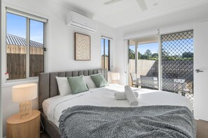 Un dormitorio con una cama grande, ventilador de techo, equipo de aire acondicionado y vistas a un espacio exterior a través de una puerta corrediza.