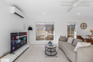 A modern living room with a flat-screen TV, a ceiling fan, and a large window. - Brand New | Modern & Comfortable | Family Friendly (Greenbank)