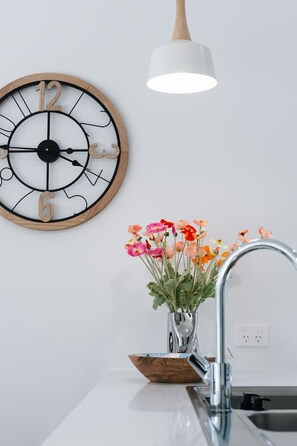 Una cocina con un reloj de madera, una lámpara colgante y un jarrón con flores.