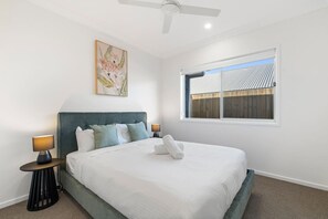 A bedroom with a bed, two bedside tables, a ceiling fan, a window with a view, and a painting on the wall. - Brand New | Modern & Comfortable | Family Friendly (Greenbank)