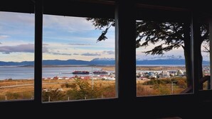 A view through a window with a landscape including mountains, a body of water, and a red ship.
